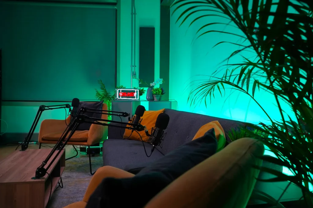 Outset Studio Shoreditch London podcast studio set up featuring a grey sofa, two yellow arm chairs, yellow cushion against an ambient green lighting backdrop