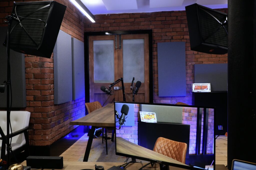 Comfortable podcast studio at Outset Studio Manchester featuring a table and brown chairs, and purple lighting against a brick wall backdrop.
