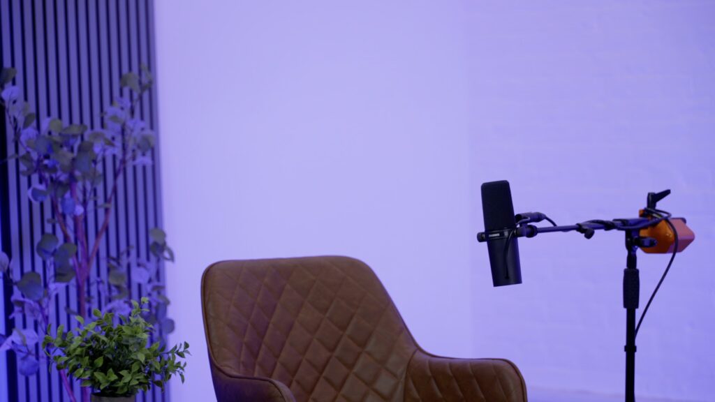 A modern podcast video studio setup a brown chair, one microphone, illuminated with purple lighting.